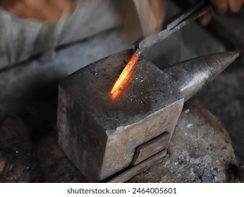 Close-up of unrecognizable person blacksmith bending wrought iron while hitting metal with hammer on anvil, The blacksmith manually forging the molten metal on the anvil in smithy with spark fireworks - Powered by Shutterstock