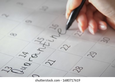 Close-up of unrecognizable person writes Quarantine with a black felt-tip pen on a calendar. Quarantine compliance. Calendar showing nothing to do except quarantine when pandemic covid-19 is raging