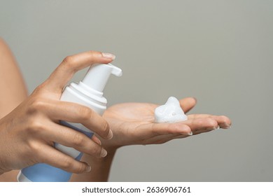 Close-up of unrecognizable person's hands using a pump mechanism to get a dollop of white, airy cosmetic lather. Concept of daily sanitation, personal treatment, or bodycare ritual.