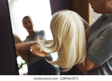 Closeup of unrecognizable woman brushing wig by mirror at home, copy space