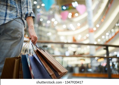 Close-up of unrecognizable woman in casual clothing standing in spacious shopping mall with lights and holding many paper bags