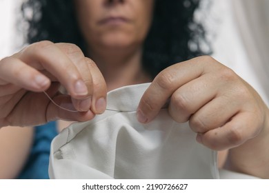 Close-up Of Unrecognizable Woman's Hands Lifting And Sewing With White Thread Her Pants To Fix Them. Woman Seamstress Doing Home Tailor Work.