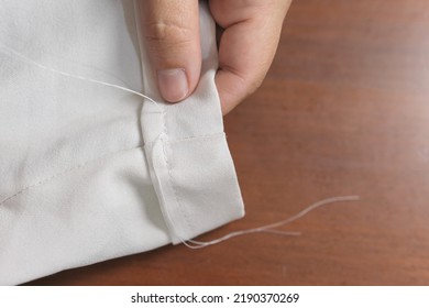 Close-up Of Unrecognizable Woman's Hands Sewing With White Thread Her Pants To Fix Them. Woman Seamstress Doing Home Tailor Work.