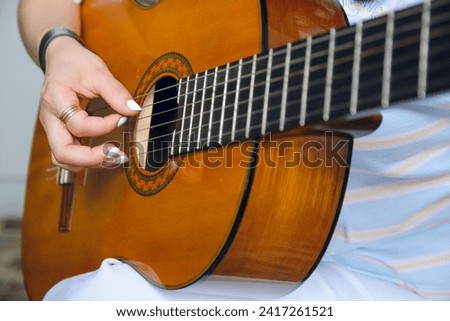 Close-up of unrecognizable young Caucasian woman playing acoustic guitar, focus on hand on strings at soundhole of acoustic guitar, copy space.