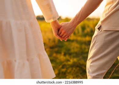 Close-up of unrecognizable young couple in love holding hands looking together to green field on sunset on beautiful summer evening. Cropped shot of wonderful romantic moment between happy couple. - Powered by Shutterstock