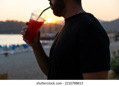 Close-up Of An Unrecognizable Young Man Drinking A Slushie Through A Straw At Sunset