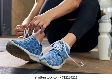 Closeup of unrecognizable young woman fixing her shoes taking break during  workout in modern gym