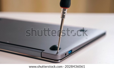 Close-up of unscrewing bolts with a screwdriver on a silver laptop.