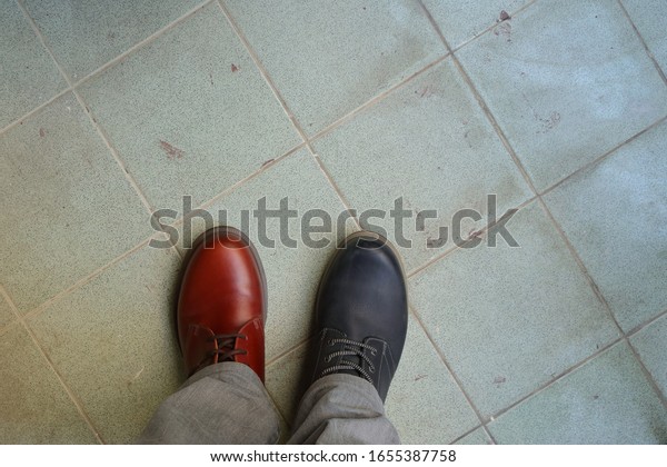 Closeup upper of mismatched shoes, a\
man wearing two different shoes and different colors standing on\
tiled floor, break the rules, revolution metaphor\
