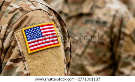 Close-up of a US flag patch on a camouflage military uniform sleeve with yellow border, blue field of white stars, and red and white stripes