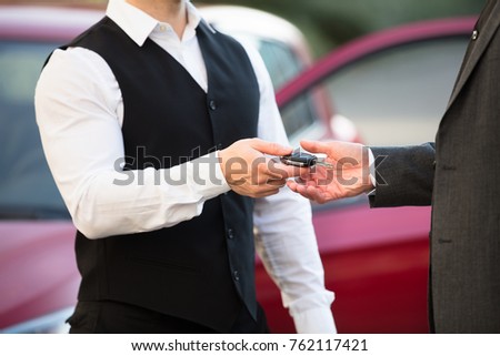 Close-up Of Valet's Hand Giving Car Key To Businessperson