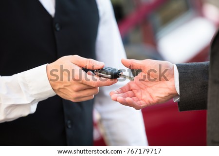 Close-up Of Valet's Hand Giving Car Key To Businessperson