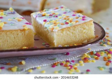 A closeup of a vanilla cake covered in frosting and sprinkles, on a white table