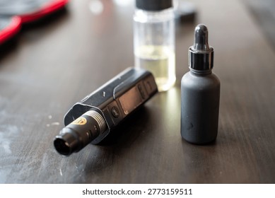 Close-up of a vaping device and two e-liquid bottles on a wooden table, showcasing vaping accessories in a casual setting.