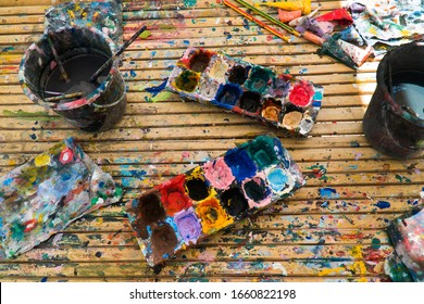 Closeup Various Of Acrylic Paint Color In Tray With Paintbrush In Water Bucket On Wood Table Background. Multicolor Of Acrylic Paint Messy In Plastic Tray With Paintbrush And Cloth On Wooden Table Art