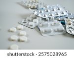 Close-up of various blister packs and white pills scattered on a white surface, symbolizing healthcare and medicine.