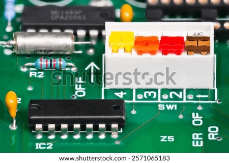 Closeup of various electronic components on printed wiring board. Colored 4 bit on-off DIP switch white package, black integrated circuits and ceramic or styroflex capacitors or resistor on green PCB.