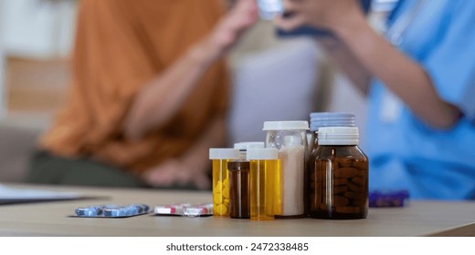 Close-up of various medication bottles and pills on table with elderly woman and caregiver in background. Concept of elderly care and medication management - Powered by Shutterstock