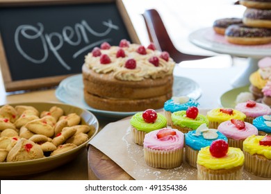 Close-up of various sweet foods on table with open signboard in cafeteria: zdjęcie stockowe