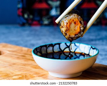 close-up of a vegan sushi rolls, una pieza de maki, held by chopsticks over a bowl of soysauce