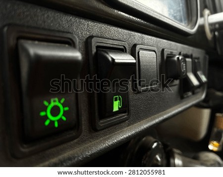 Close-up of vehicle dashboard control panel with illuminated green indicator lights for headlights and fuel gauge functions.