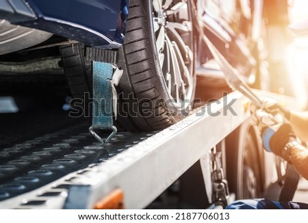 Closeup of Vehicle Wheel Secured on the Tow Truck with Tie Down Straps for Safe Transportation. Breakdown Assistance. Automotive Industry.