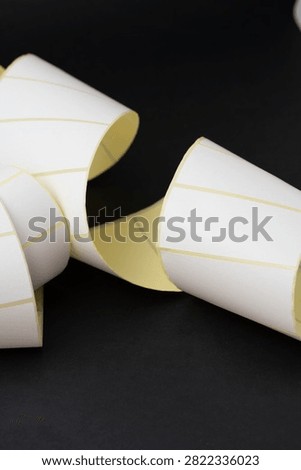 Close-up vertical composition of curled blank white adhesive labels with yellow backing on black.