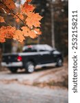 Close-up of vibrant autumn leaves with a blurred pickup truck in the background, capturing the essence of fall and outdoor adventure with a subtle automotive presence.