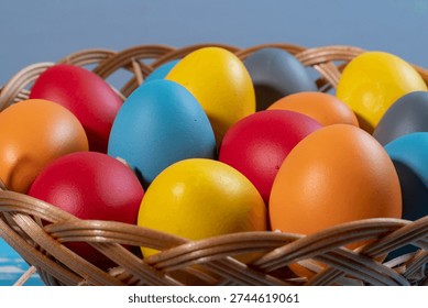 Close-up of vibrant Easter eggs in different colors arranged inside a wicker basket, symbolizing spring celebration and traditional holiday decoration.