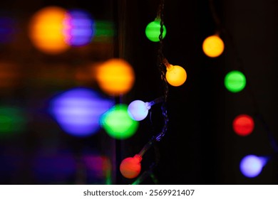 Close-up of vibrant, multicolored string lights glowing in the dark, creating a festive and cozy atmosphere. Defocused lights add depth and bokeh effect