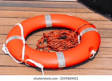 Close-up of a vibrant orange life ring equipped with a tied rope placed on a wooden dock, photographed under bright daylight, emphasizing safety equipment and maritime concepts. - Powered by Shutterstock