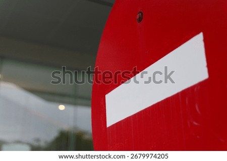 Close-up of a vibrant red circular do not enter sign featuring a prominent white horizontal bar, symbolizing prohibition and restricted access, against a blurred background.