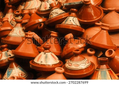 A close-up of a vibrant stack of traditional Moroccan tagines and terracotta pots displayed at a market, featuring both plain and painted designs.