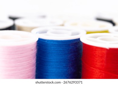 Close-up of vibrant thread spools in pink, blue, red, and yellow. Sewing threads are neatly arranged on a white surface, creating a colorful pattern.