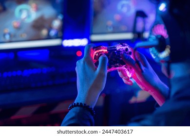 Close-up, video game console controller in gamer hands at colorful neon light living room at night, E-sport streaming game online, selective focus - Powered by Shutterstock