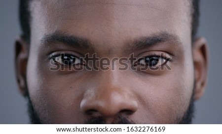 Close-up view of afro-american man eyes blinking and looking straight. Detailed portrait of confident and calm black guy staring at camera.