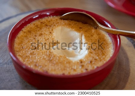 Close-up view of Crème brûlée (also known as burnt cream or Trinity cream) in red ramekin standing on wooden table. Soft focus. Desserts theme.