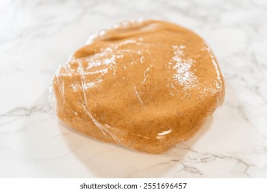 Close-up view of the Amber Gingerbread Cookie Dough wrapped in plastic wrap, shaped into a flat disc for even chilling in the refrigerator. The wrapping preserves freshness and prepares the dough for - Powered by Shutterstock