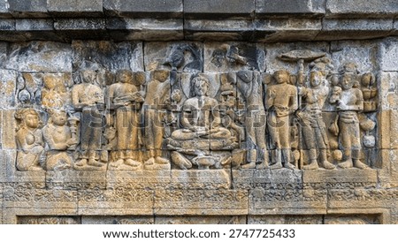 Closeup view of ancient stone bas-relief of Buddha sitting on lotus throne with worshippers, Borobudur buddhist stupa, Magelang, Java, Indonesia