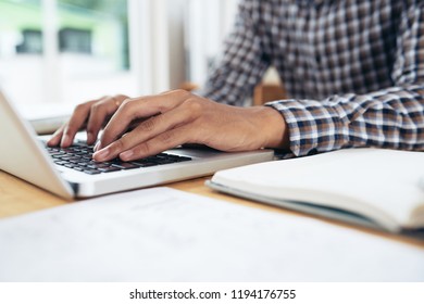 Close-up view of anonymous man in checked shirt sitting at table and typing on notebook