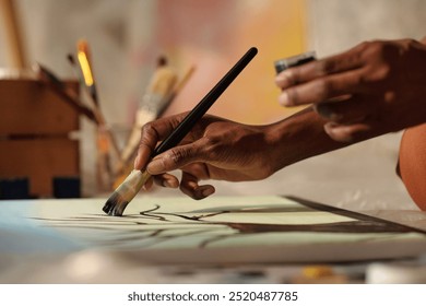 Close-up view of artist's hand holding paintbrush while painting on canvas with brushes and tools around - Powered by Shutterstock