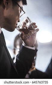 Close-up View Of Asian Businessman In Eyeglasses Drinking Whiskey From Glass