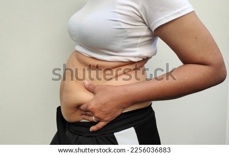 Close-up view of Asian woman is beside belly. Wearing a white shirt. There is a lot of excess fat. Seeing the fat groove until the belly sags. Holding both hands. Dimpled navel and weight loss concept