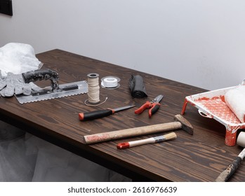 close-up view of assorted hand tools and supplies laid out on a woodgrain table, ready for painting, cutting, and building tasks, representing typical renovation or repair preparation