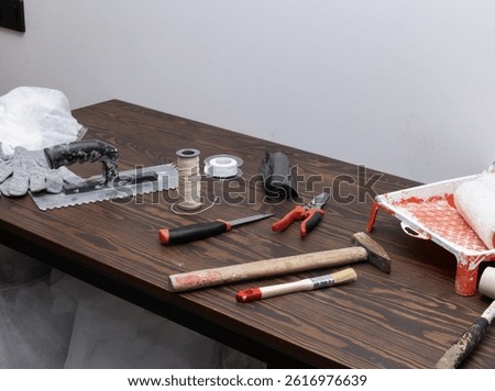 close-up view of assorted hand tools and supplies laid out on a woodgrain table, ready for painting, cutting, and building tasks, representing typical renovation or repair preparation