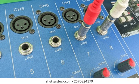 Close-up view of an audio mixer showing input channels with microphone and line level jacks and cables plugged in.
