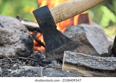 Closeup view of axe with a wooden handle embedded in a log of wood, with a campfire in the background, survival or historical recreation, leisure activities and relaxation around a fire - Powered by Shutterstock