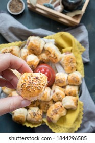 Closeup View Of A Baked Homemade Sausage Roll Held By A Woman Hand Over A Blurred Dish Full Of Sausage Just Baked Rolls.