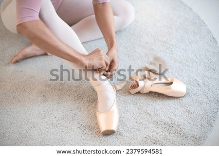 Close-up view, Ballerina sitting on the floor and tying ribbons of ballet pointe shoes, prepares for a rehearsal at home