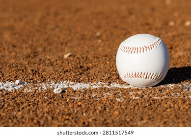 Close-up view of a baseball on a baseball field's dirt infield, with a white foul line marking the boundary